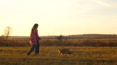 Anne ve kızı ile onların sevgili köpeği günbatımında yürüyor. Ağır çekim