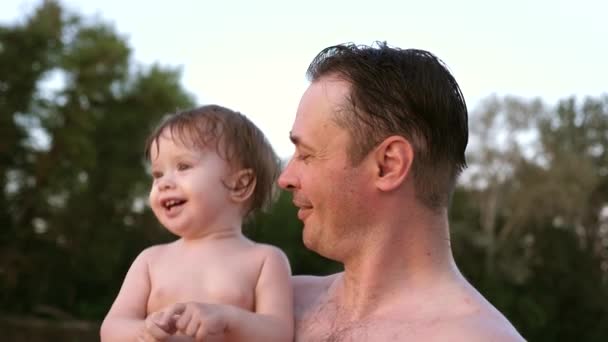Small wet bathing child claps his hands and laughs sitting in embrace of dad — Stock Video
