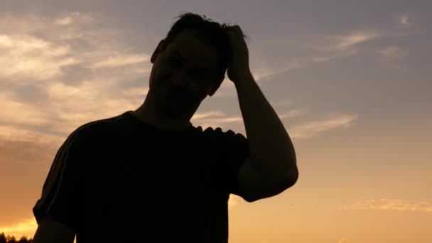 Silhouette eines Mannes, der seinen Kopf gegen den Sonnenuntergang kratzt — Stockvideo