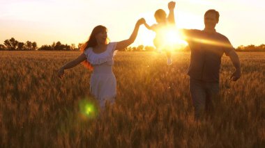 Anne ve baba ile ışınları golden sunset ve gülüyor buğday alanında yürüyüş ile mutlu bir çocuk. Oynama ve buğday alanı gülümseyen anne ile bebek.