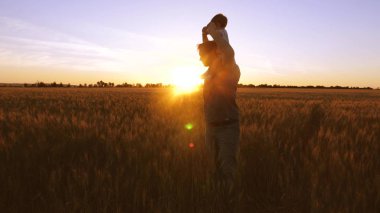 Baba küçük bebek onun omuzlarında taşıyan ve buğday alanında altın günbatımı çerçevede gülüyor.