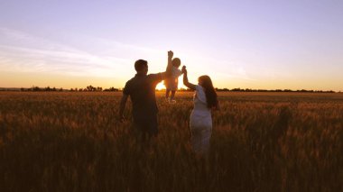 Çocuk ailesi ile alan golden sunset ışınlarının buğday ile yürür. Bebek anne ve baba oynamak ve buğday alanıyla gülmek.