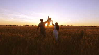 Çocuk ailesi ile alan golden sunset ışınlarının buğday ile yürür. Bebek anne ve baba oynamak ve buğday alanıyla gülmek.