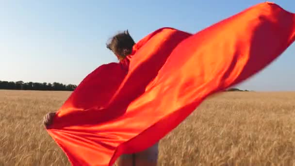 Mavi gökyüzü karşı kırmızı pelerin buğday ile araziyi çalışan kız süper kahraman. Ağır çekim