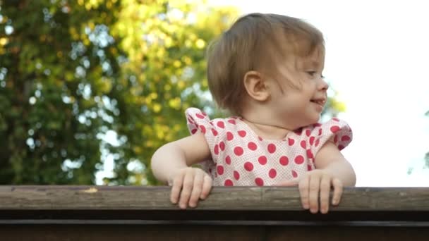 Pequeno bebê feliz sorrindo com os primeiros dentes de bebê jogando no banco no parque no fundo do bokeh — Vídeo de Stock