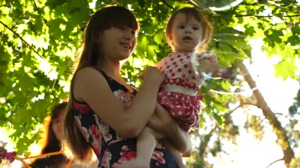 Mãe e sua filhinha estão pegando bolhas de sabão grandes e transparentes no parque da cidade — Vídeo de Stock