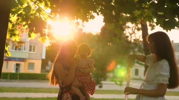 Mamma e le sue figlie catturano grandi e trasparenti bolle di sapone nel parco cittadino e ridono in bagliore di sole — Video Stock