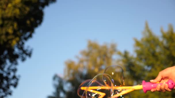 Девушка надувает большие пузыри в городском парке против голубого неба. Крупный план. Медленное движение — стоковое видео