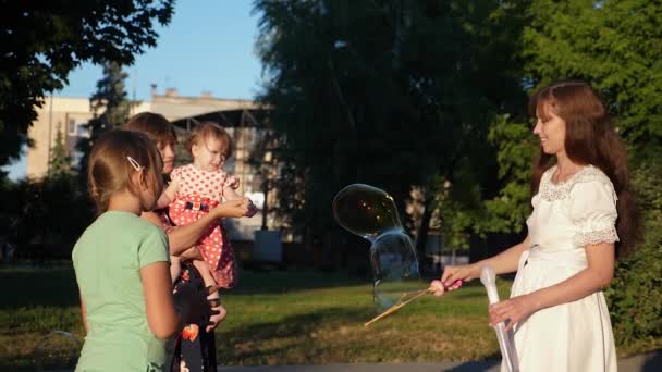 Moeder en kinderen zijn het maken van enorme zeepbellen in stadspark en lachen. Slow motion — Stockvideo