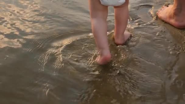 Criança caminha na água na praia com sua mãe, salpicando água ao redor, câmera lenta — Vídeo de Stock