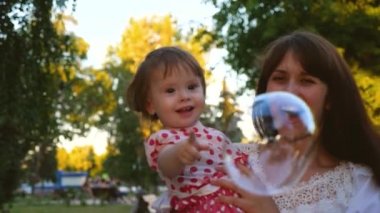 Küçük bebek ile anne büyük şeffaf sabun köpüğü, gülüyor ve gülümsüyor elleriyle patlamaları. Ağır çekim