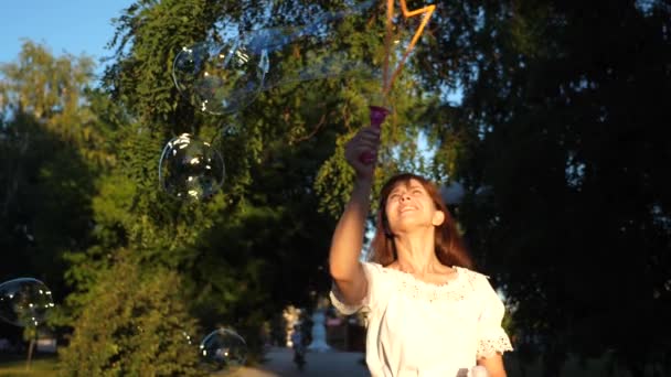 Menina alegre ri e lança grandes bolhas de sabão no parque da cidade e sorri. Movimento lento . — Vídeo de Stock