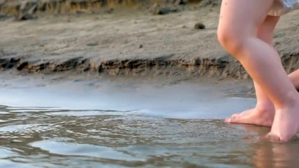 La mano de las mamás lleva al niño a la playa. pies de niño van en el agua. En cámara lenta. de cerca . — Vídeos de Stock