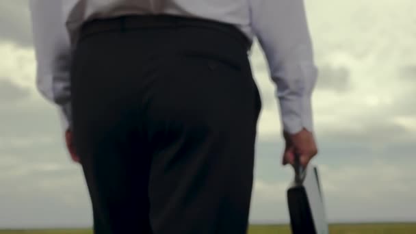 Businessman is walking along field with briefcase in his hand against background of dark clouds — Stock Video