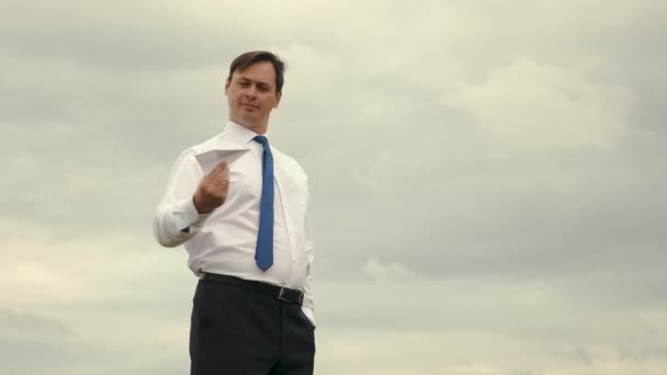 Empresario en camisa blanca y corbata está jugando con el avión volador de papel contra el fondo de nubes oscuras — Vídeo de stock