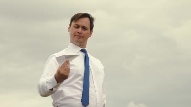 Uomo d'affari in camicia bianca e cravatta sta giocando con carta volante aereo sullo sfondo di nuvole scure — Video Stock