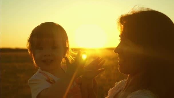 Feliz niño aplaude, sentado en las manos de una madre risueña al atardecer del sol dorado. Movimiento lento . — Vídeos de Stock