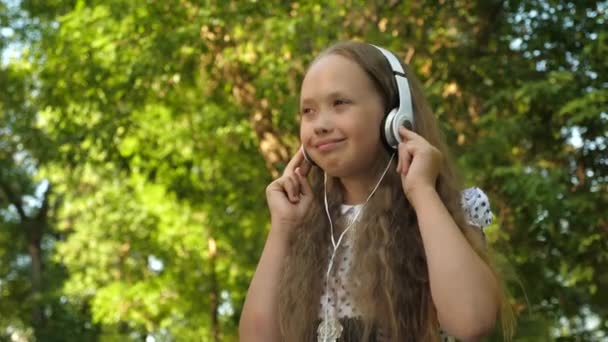 Chica en auriculares escuchando música y bailando sonriente en el parque de verano — Vídeos de Stock