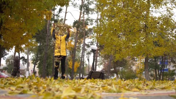 L'adolescente lancia foglie gialle verso l'alto e sorride in un parco autunnale. Rallentatore — Video Stock