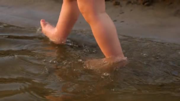 El pequeño bebé en pañal da sus primeros pasos caminando a lo largo de la orilla del río. Piernas. Primer plano. Movimiento lento — Vídeos de Stock