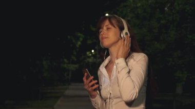 Kız kulaklık ve fener ışığı altında gece şehirde gülümseyerek dans müzik dinlemek dokunmatik telefon