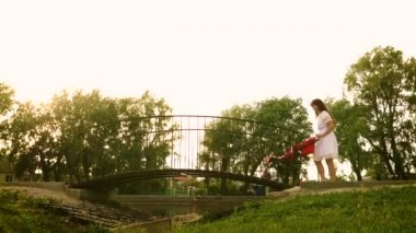 Anne Bebek arabasındaki bebek Parkı ile yaz aylarında yürüyor, Genç Anne köprü gezginci üzerinde haddeleme