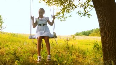 Uzun saçlı Genç kız bir meşe ağacının altında bir salıncak üzerinde sallanır. Ağır çekim.