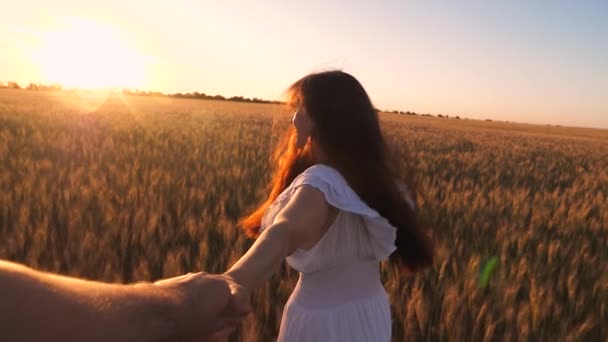 白いドレスの少女は黄金の太陽の輝きの手で彼女の最愛の人を保持している小麦でフィールド間で実行されます。スローモーション. — ストック動画