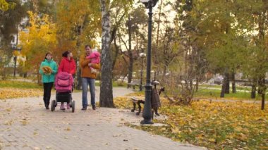 Genç aile çocuk ve bebek arabası ile parka giderken yol gösterir. Ağır çekim.