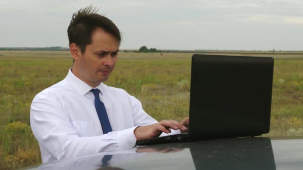 Empresário em camisa branca e gravata escreve texto no teclado do laptop no telhado do carro — Vídeo de Stock