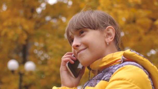 Nastoletnie dziewczyny rozmowy na telefon w jesienny park i uśmiechając się. — Wideo stockowe