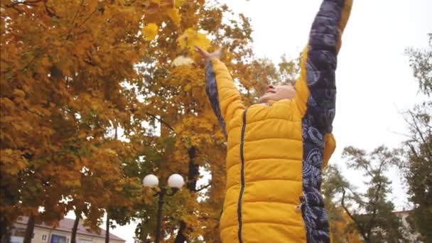 Menina alegre lança folhas amarelas no Parque no outono e sorri. Movimento lento. Menina descansando no parque no outono . — Vídeo de Stock