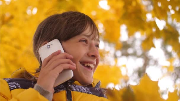 Adolescente hablando por teléfono en un parque de otoño y sonriendo. Movimiento lento . — Vídeos de Stock