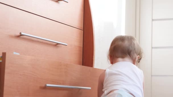 Маленький ребенок ползает по полу и забирается в шкафы, играя в детской комнате . — стоковое видео