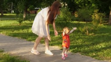 Bebek annesi el ve Park'ta yürüyordunuz tutan ilk adım atıyor. Anne yürüyen küçük kızı güler.