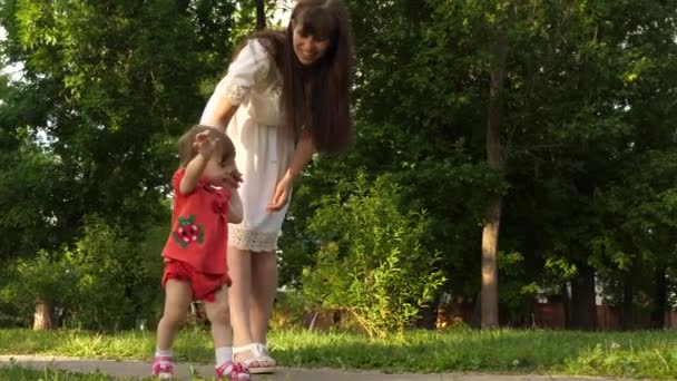 El bebé da los primeros pasos cogiendo a su madre de la mano y caminando en el parque . — Vídeo de stock