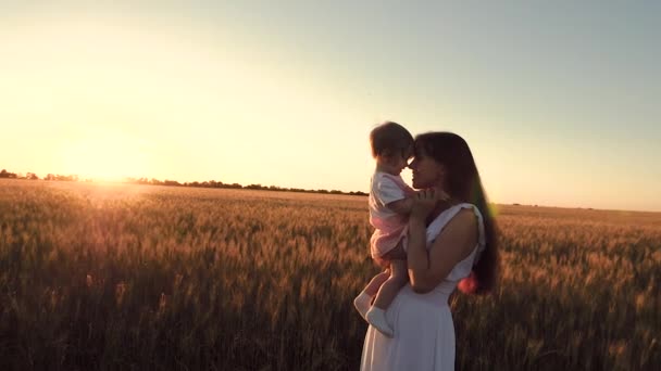 Kleine baby met haar moeder gaat naar het tarweveld en lacht tegen de achtergrond van een gouden zonsondergang. Slow motion. — Stockvideo