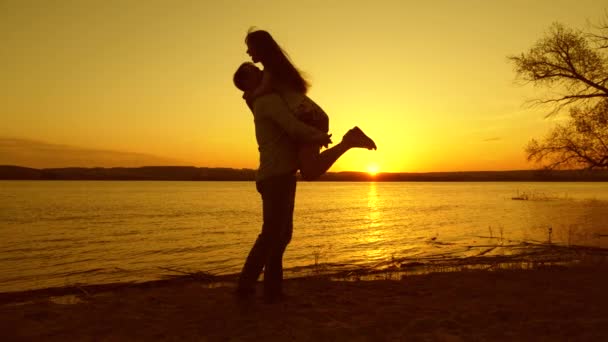 Enamorado de la muchacha y el hombre bailando en la playa por la tarde en los rayos de la puesta de sol amarilla — Vídeo de stock