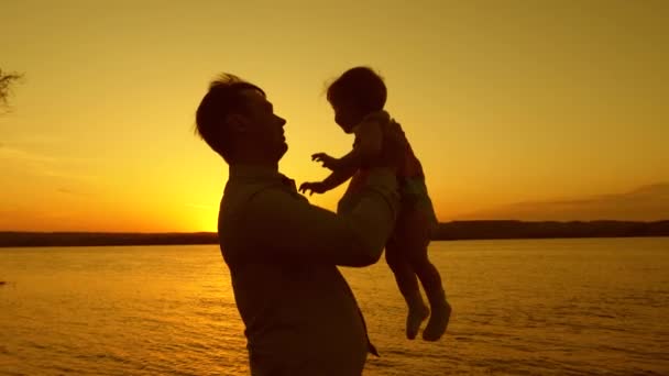 Papa spielt und tanzt mit seiner kleinen Tochter auf einem gelben Sonnenuntergang an einem schönen See. Nahaufnahme — Stockvideo