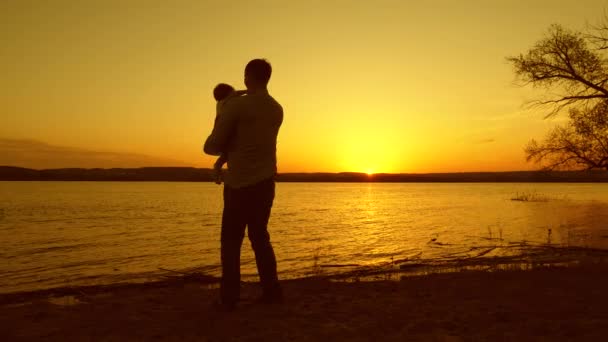 아빠는 재생 하 고 그의 작은 딸과 함께 따뜻한이을 저녁에 아름 다운 호수에 대 한 노란색 일몰에 춤. 클로즈업 — 비디오