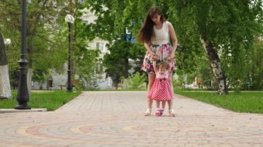 Gün boyunca yeşil parkta yürüyüş anne elinde tutmak için ilk adımlarını yapmaya mutlu bebek.