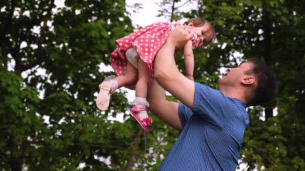 Young dad and baby laughing together while playing outdoors. Girl is jumping in air at hands of parent and smiling. Slow motion. — Stock Video