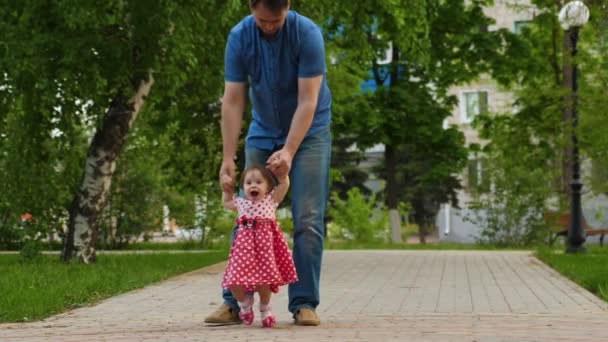 Vader leidt kleine baby op weg naar het park. Jong geitje leert om te lopen. Ouder met kind op wandeling — Stockvideo