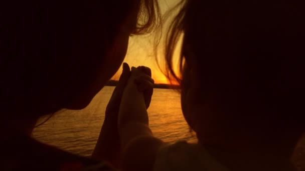Mutter und Tochter bewundern den schönen Sonnenuntergang. Kind in den Händen einer jungen Mutter bei Sonnenuntergang goldene Sonne. — Stockvideo