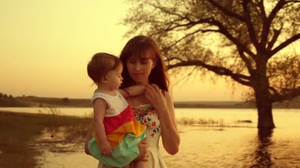 Мама и дочь прогуливаются вдоль пляжа у озера на закате. счастливый ребенок на руках у мамы — стоковое видео
