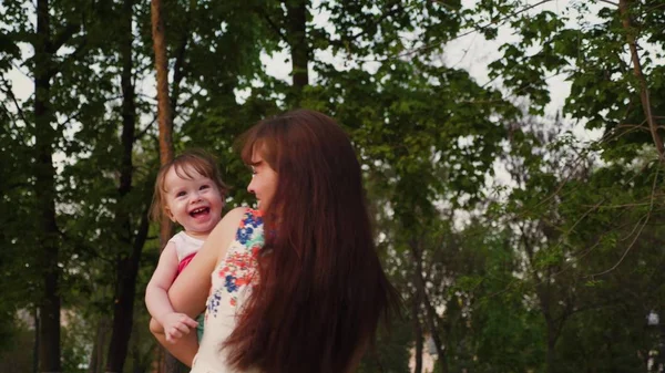 Young mother plays in the park with a small baby laughing and shaking it in her arms. — Stock Photo, Image