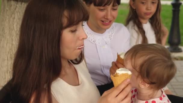Menina está comendo sorvete sentado no banco no parque com sua família . — Vídeo de Stock