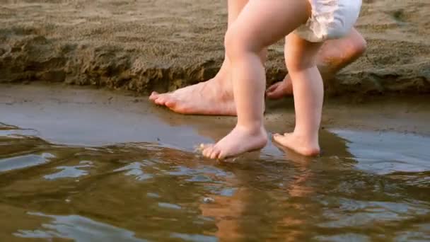 Moms hand leads kid on beach. feet of child go on the water. Slow motion. close up. — Stock Video