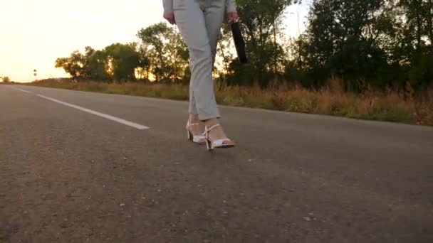 Pies de mujer en zapatos y pantalones blancos están en asfalto. mujer de negocios lleva un maletín negro en la mano, vista desde la parte trasera. vista frontal — Vídeos de Stock