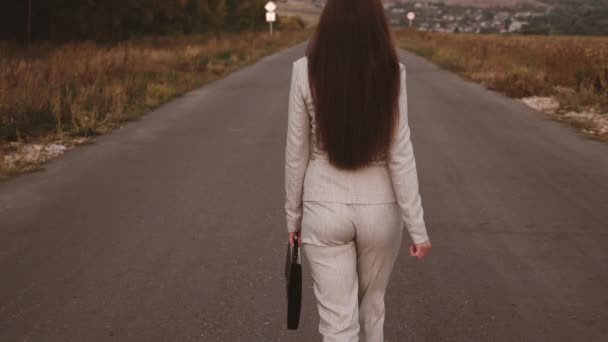 Esbelta mujer de negocios con maletín negro en la mano va en pantalones y zapatos blancos de tacón alto en el asfalto, vista trasera — Vídeo de stock